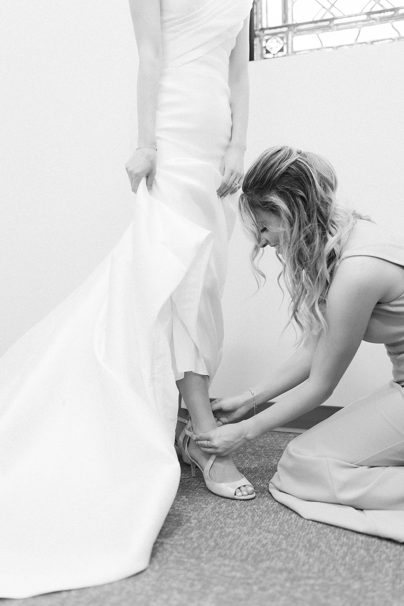 bridesmaid helps bride with shoe before Raleigh NC wedding