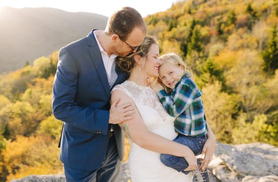 A couple celebrates their 5 year anniversary in their wedding attire with their child on Rough Ridge in North Carolina