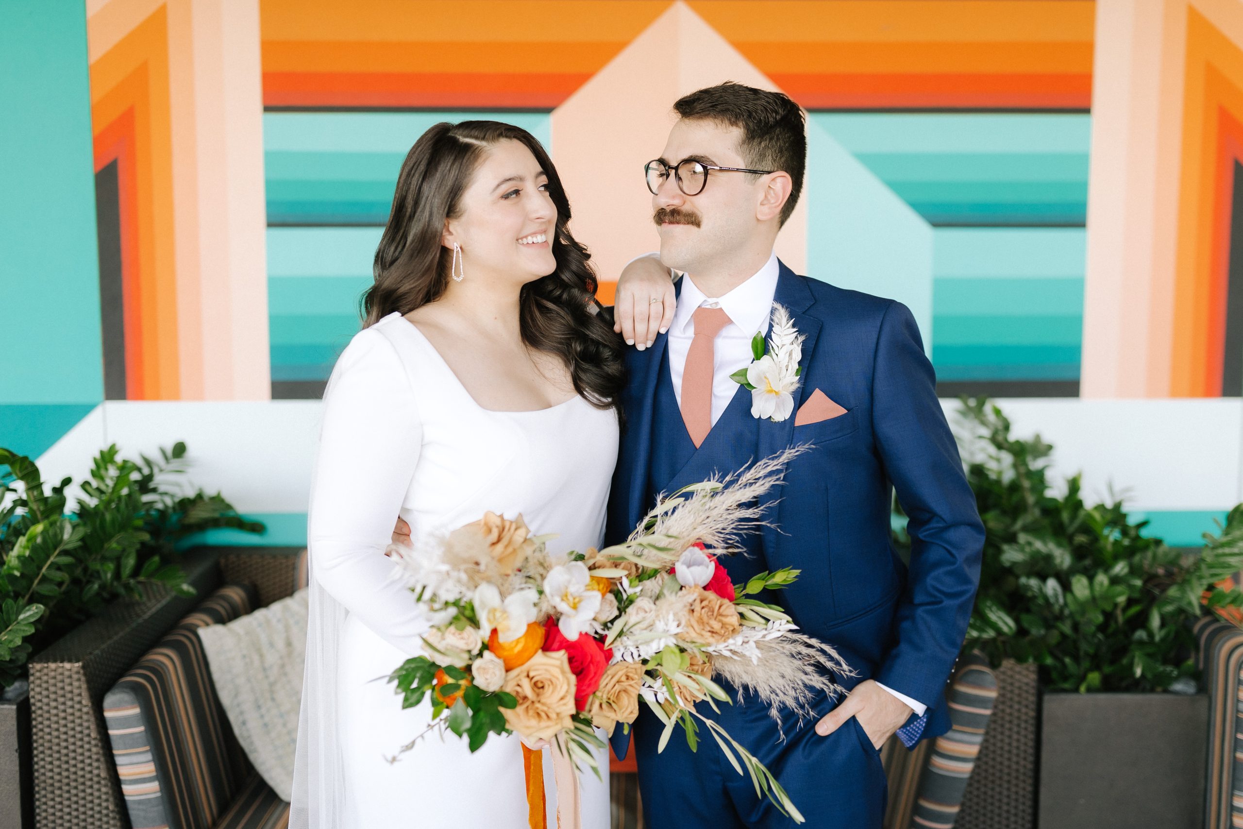couple stands in front of a colorful wall during their first look at this Tampa greek orthodox wedding