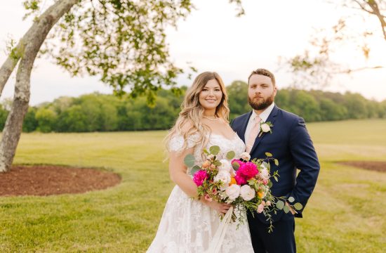 A couple stands together with a colorful floral arrangement on their wedding day at Board & Batten Events in Lexington, NC